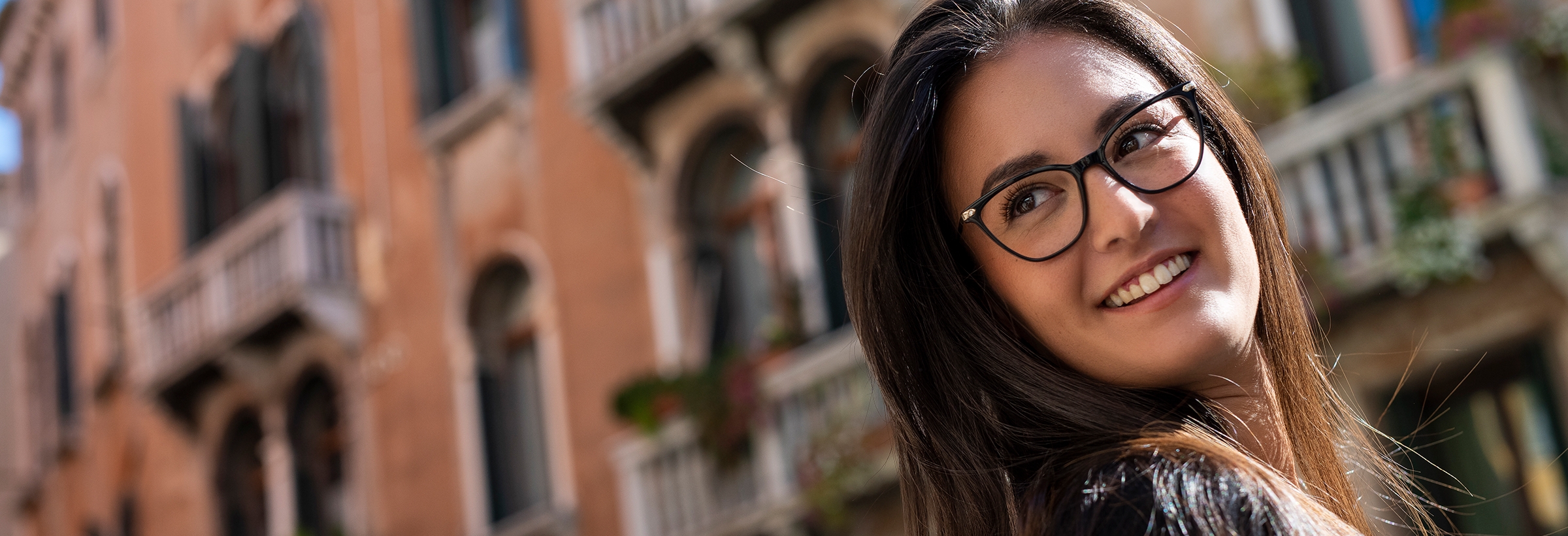 A smiling woman strolling around an Italian town wearing Arlecchino glasses