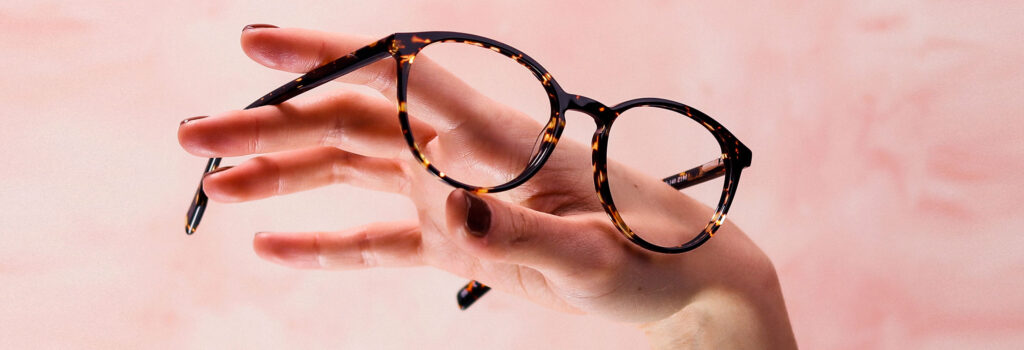 Pair of round tortoiseshell frames balancing on a female's hand facing to the right