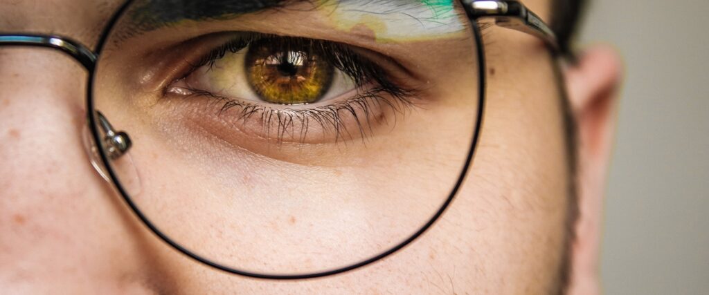Close-up of a dark amber eye seen through a pair of round black metal frames