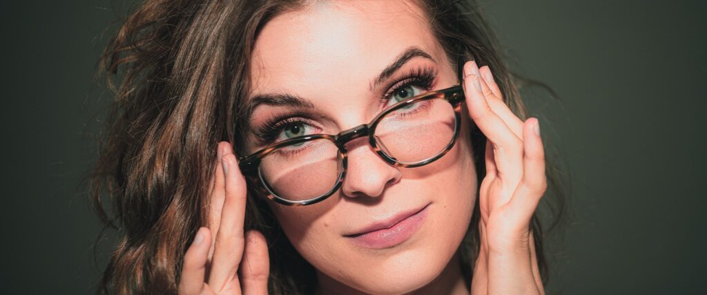 A woman with grey-green eyes looks over the rims of her round tortoiseshell glasses