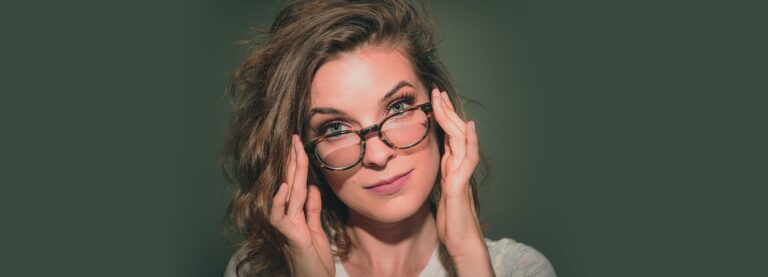 Female with green eyes wearing glasses pulling the frames slight down