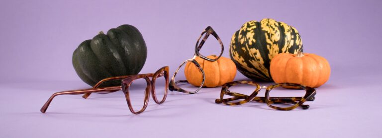 3 pairs of glasses in different angles leaning on pumpkins on a purple background