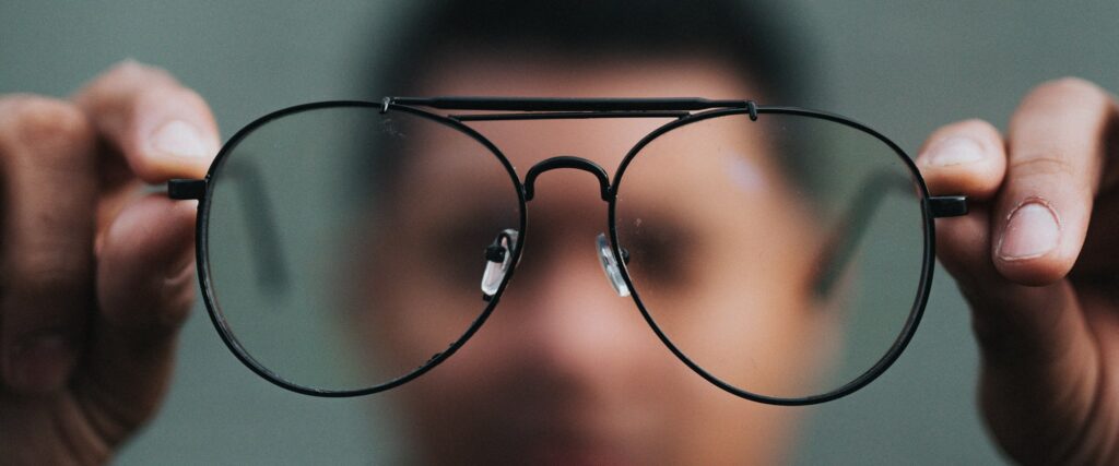 Close-up of black metal aviator glasses held up by man with background blurry