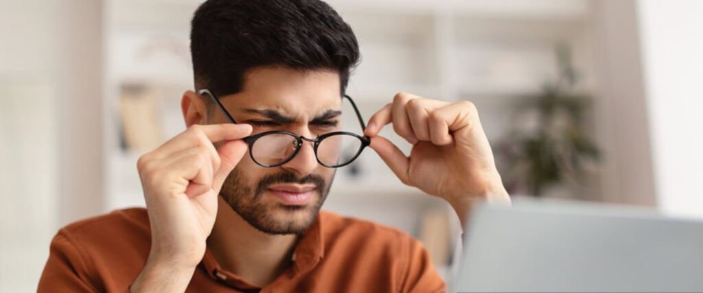 Man squinting whilst looking at a laptop screen