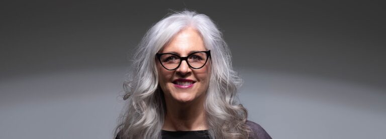 Older woman with white hair smiling while wearing cat-eye frames