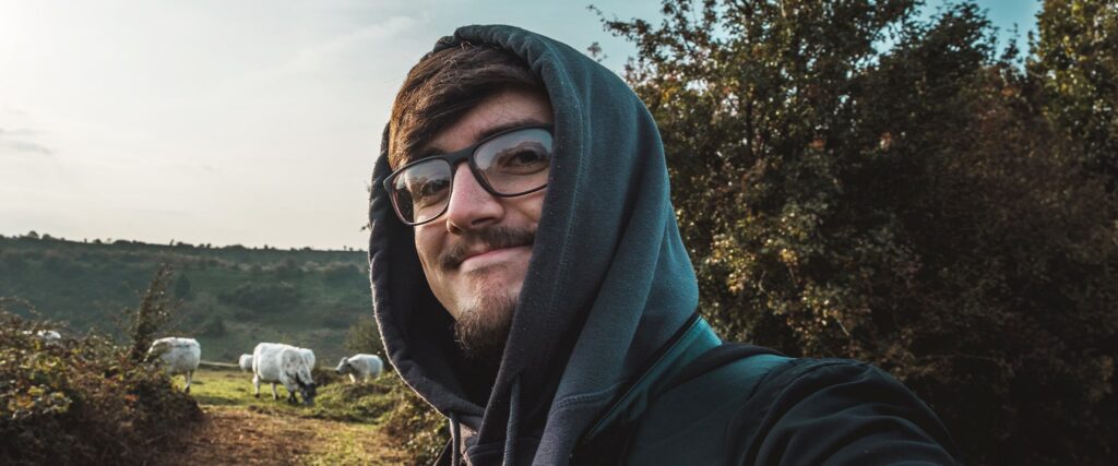Man outdoors wearing rectangular frames posing for a selfie smiling