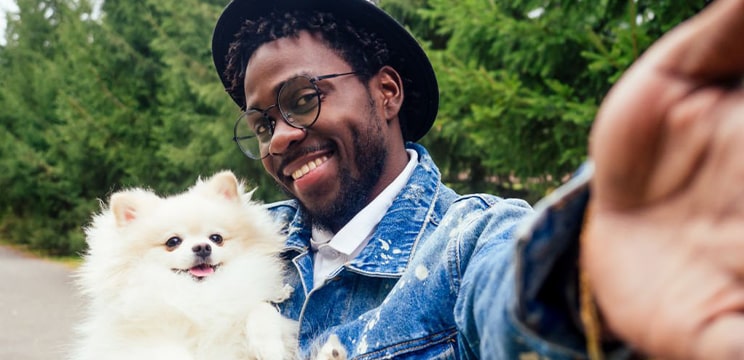 Man wearing round glasses smiling while posing with his pet dog for a selfie
