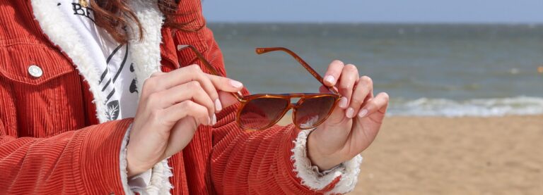 Lady wearing a coat holding up a pair of sunglasses