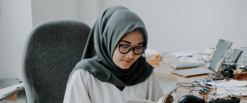 Woman wearing a grey hijab and black glasses reading a book