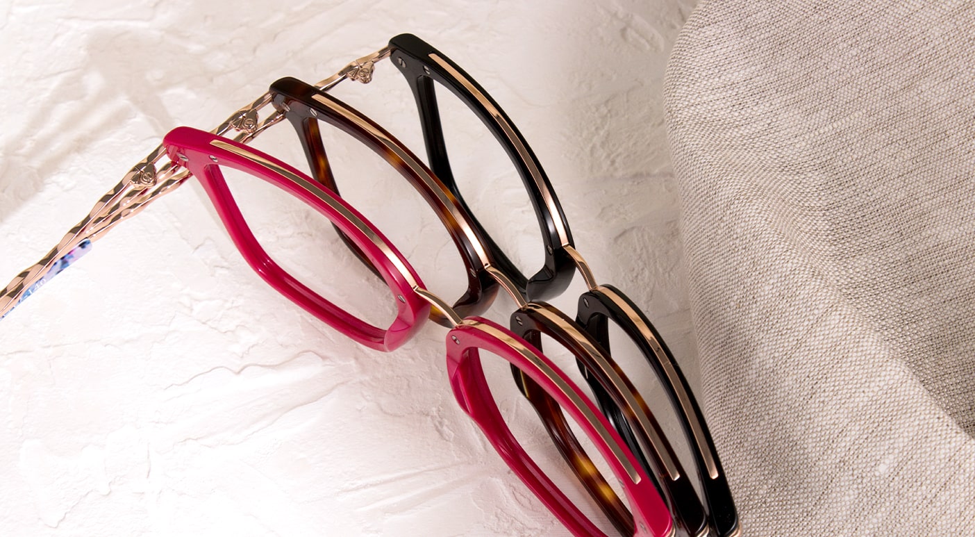 Three pairs of Scout Made in Italy frames, one tortoiseshell, one pink and one black overlapping on another on fabric sheet