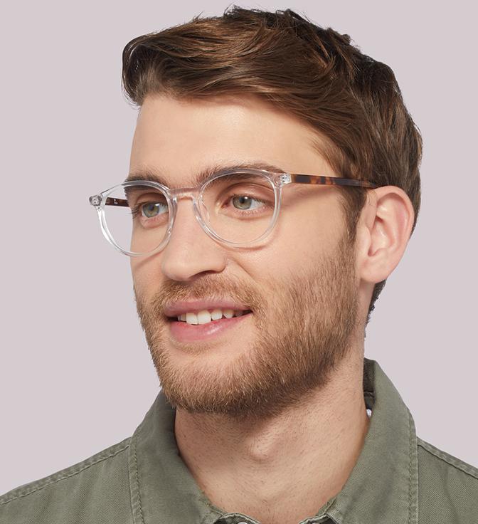 Image shows a man wearinf clear frames with a tortoiseshell pattern on the arms, with a light pink background.