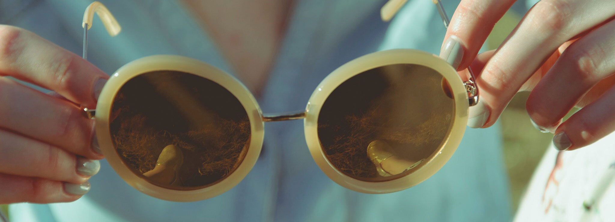 Image of woman holding a pair of round, yellow sunglasses.