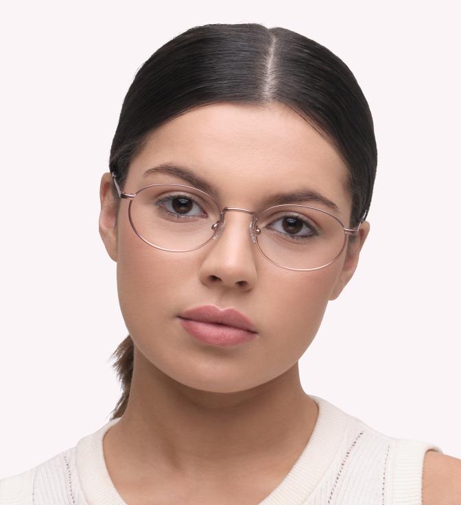Image showing a woman wearing oval, rose gold metal frames with a light pink background.