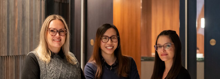 Three women working on the Glasses Direct team smiling and laughing in an office hallway