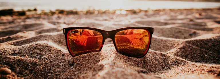 Close-up of a pair of sunglasses with orange lenses on a beach