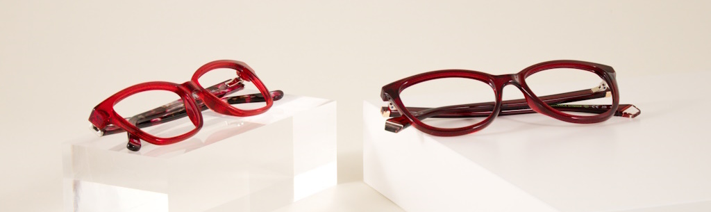 Two red glasses frames made of plastic lying on top of elevated white pedestals