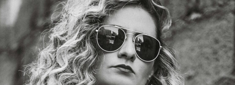 Black-and-white close-up of a blonde woman with curly hair wearing aviator sunglasses