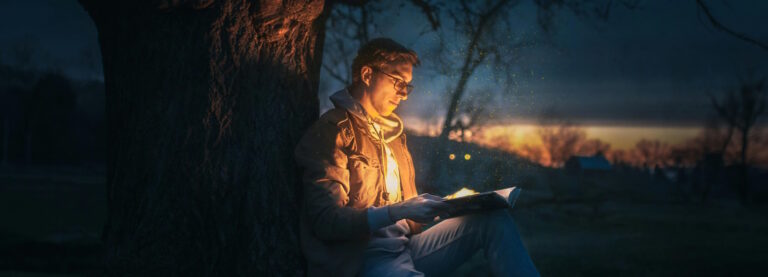 A man reading a book under a tree. The sun has almost set and it's dark, but a magical glow emanates from the book and illuminates the immediate area.