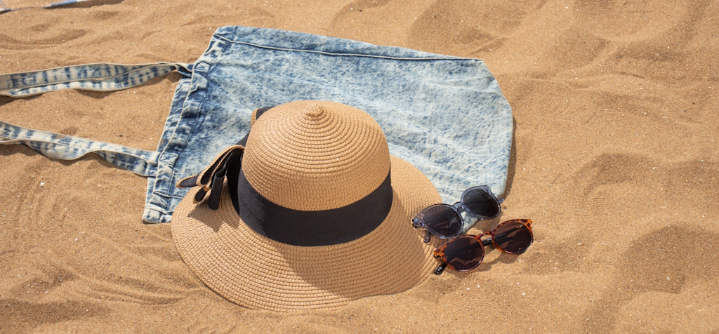 A beach bag, a sun hat and two pairs of sunglasses lying in the sand on a beach