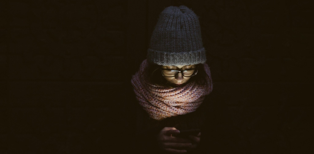 A woman in warm winter clothes looking at her phone in the dark