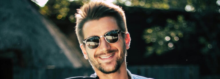 Smiling man with a short beard wearing Clubmaster sunglasses outdoors